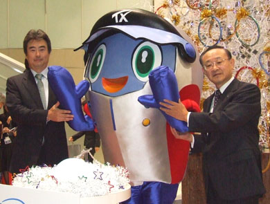 インテルの吉田社長（左）とTXの高橋社長。中央はTXマスコットの「スピーフィ」君